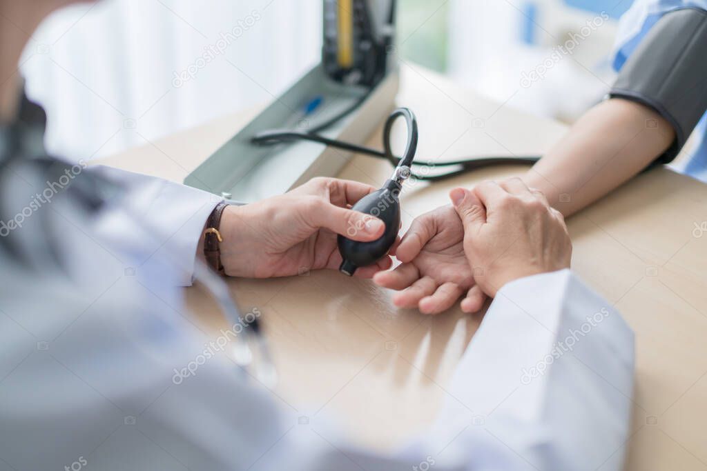 health ideas concept with close up Doctor hand  using sphygmomanometer with stethoscope checking blood pressurefor asian woman patient in the hospital background