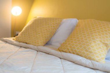 Yatak odasındaki yumuşak, sarı yastıklı güzel tasarım konsepti.