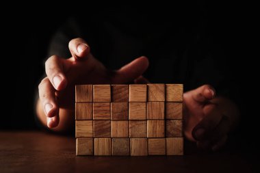 İşadamı, tahta masa ve siyah arka plan iş organizasyonu kavramında diğerlerinden tahta bloğu seçmeye çalışır.