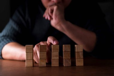 İşadamı, tahta masa ve siyah arka plan iş organizasyonu kavramında diğerlerinden tahta bloğu seçmeye çalışır.