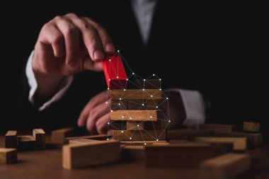 İşadamı ahşap masa üzerine ahşap blok inşa etmeye çalışıyor ve siyah arkaplan iş organizasyonu başlangıç konsepti