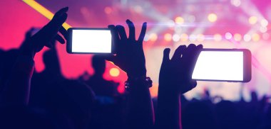 Sosyal medya kavramı, insanların ellerinde akıllı telefon görüntüsü, soyut bulanık arka planlı renkli ışıklandırma konser olayında heyecan verici bir an.