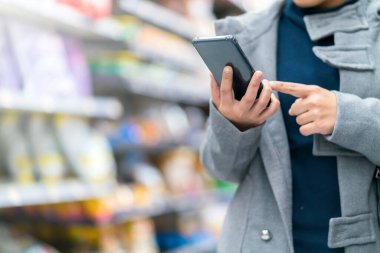 Yakın plan Asyalı kadın el bilgisayarı. Akıllı telefon kontrol fiyatları süpermarket fiyatlarıyla market alışveriş kartı ve sıra sıra ürünler karşılaştırılıyor.