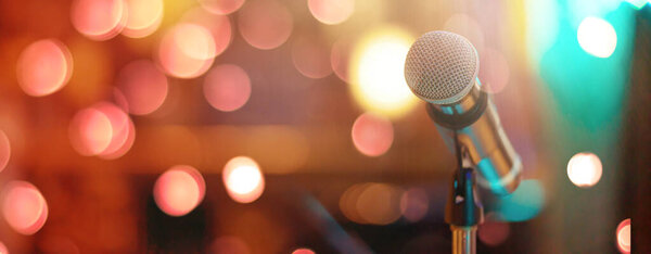 Close up of high fidelity microphone setting on stand with colorful abstract light bokeh background in conference seminar hall . Microphone on stage banner size.