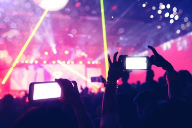 Sosyal medya kavramı, insanların ellerinde akıllı telefon görüntüsü, soyut bulanık arka planlı renkli ışıklandırma konser olayında heyecan verici bir an.