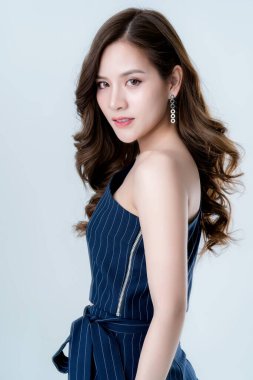 Güzel, çekici, zarif, mavi elbiseli Asyalı bir kadın, el ele tutuşan bir model, stüdyo fotoğrafında poz veriyor, beyaz arkaplanı ayırıyor.