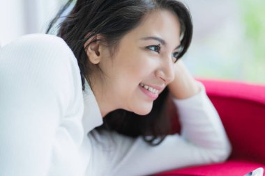 Akıllı, çekici, beyaz bir kadın. Akıllı telefon keyfine bakar. Kırmızı koltukta rahat bir hafta sonu.