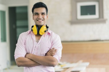 Gözlüklü ve kulaklıklı akıllı Hintli marangoz müteahhidi iç dekorasyon konsepti için beyaz tavanı kontrol et.