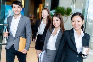 Bir grup zeki Asyalı iş adamı ve kadın resmi kıyafet modern ofis girişinden güven ve mutlulukla geçiyorlar.