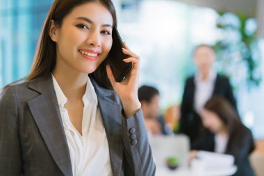 Zeki, çekici Asyalı iş kadını, gülümseyen el modern ofis geçmişine sahip akıllı telefonu tut.