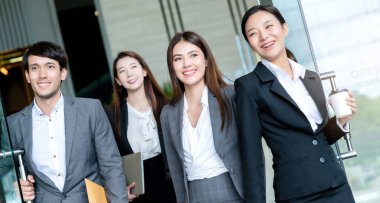 Bir grup zeki Asyalı iş adamı ve kadın resmi kıyafet modern ofis girişinden güven ve mutlulukla geçiyorlar.