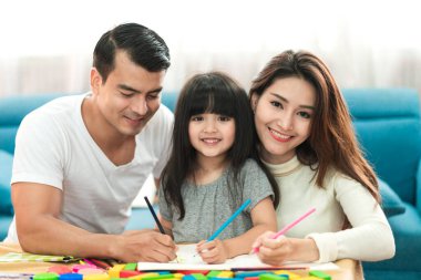 Şirin siyah saçlı kız çocuk, ev ödevi ve ebeveyni ile birlikte oturma odası konseptine gülmek.