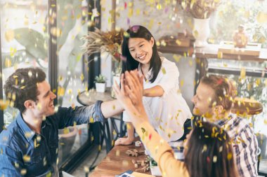 Çok uluslu iş arkadaşlarıyla el gücü ve konfeti kağıtlarıyla mutluluk ve neşe dolu başarılı bir zafer buluşması.