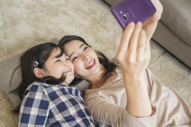 Mutlu Asyalı Aile Anne ve Kızı oturma odasının arka planında selfie çekiyorlar..