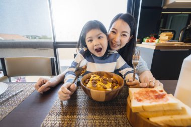 Mutlu Asyalı anne ve kız mısır gevreğinin tadını çıkarın. Sağlıklı yemek konsepti yemek odası arka planı.
