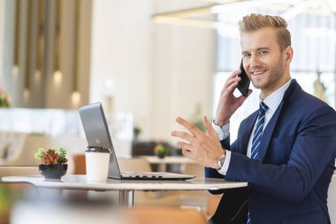 Zeki, beyaz takım elbiseli iş adamı laptopla ve mutlulukla akıllı telefon iletişimiyle çalışıyor ve başarılı iş fikirleri kavramına odaklanıyor.