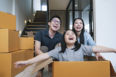 Mutlu Asyalı aile, anne, baba yeni eve taşınan kız, mutlu ve neşeli ifadeli bir kutu eşya taşıyor.