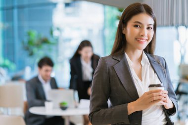 Zeki, çekici, Asyalı iş kadını, gülümseyen el, modern ofis geçmişine sahip sıcak bir içecek.