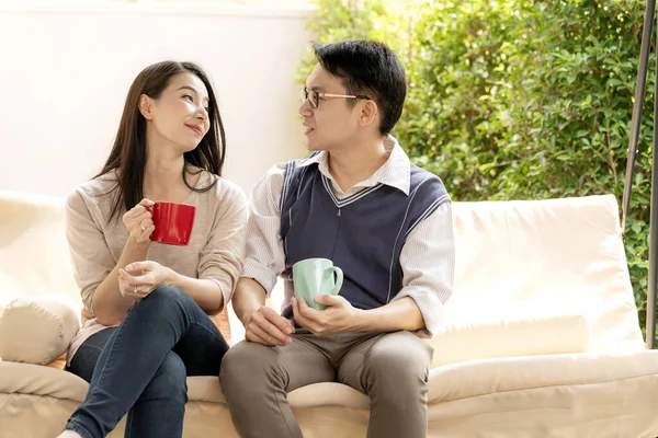 sweet and lovey asian couple husband and wife with hot drink talk together with happiness and peaceful home interior background