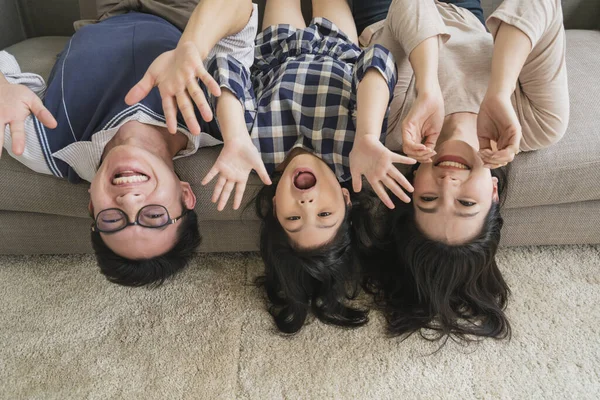 happy Asian Family mother father and daughter making a fun sleep upside down on sofa  living room home background.