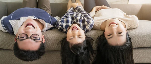 happy Asian Family mother father and daughter making a fun sleep upside down playing on sofa  living room home interior background.