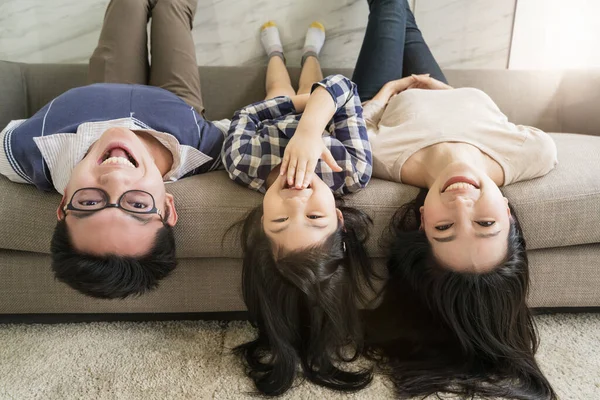 happy Asian Family mother father and daughter making a fun sleep upside down on sofa  living room home background.