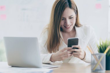 İş kadını Asyalı rahat vakit geçirmeyi sever. Akıllı telefona gülümseme ve mutlulukla dokun.