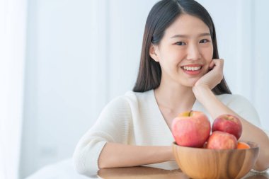 Sağlıklı beslenme konsepti güzel Asyalı kadın gülümse el ahşap kasede taze elma göster mutluluk ve neşeli beyaz oda arka planı