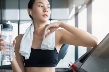 Spor salonundaki koşu bandında duran bitkin Asyalı kız rahatla ve sağlıklı fikirler kavramını sakinleştir.