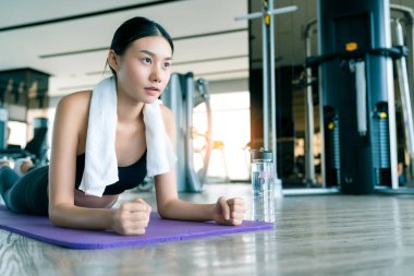 Genç güçlü Asyalı kadın spor salonunun arka planında kalas egzersizi yapıyor.