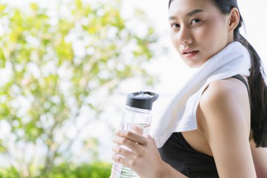 Güzel Asyalı kadın eli yoga minderi ve su şişesi tutuyor. Sağlıklı spor için yoga yapıyor. Bahçe geçmişi var.