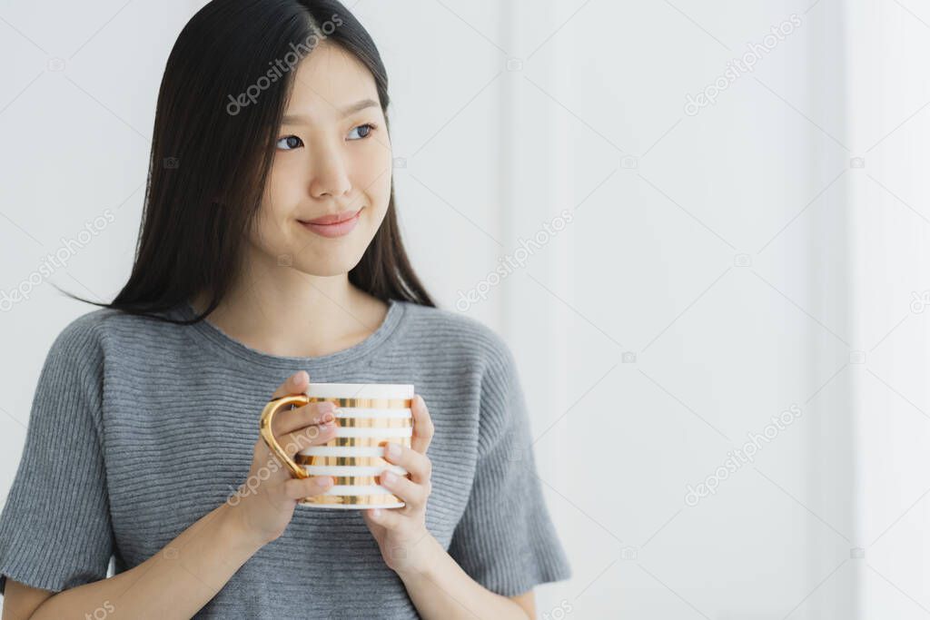 beautiful asian teen  white Tank top happiness smile enjoy freshness morning with hot drink near window with sun light