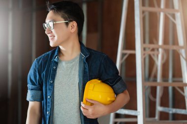 Ev dekorasyonunda çalışan Asyalı çekici gözlüklü iç mimar. Gülümsemesi ve kendine güveni olan, mavi baskı ve çizim aracıyla birlikte çalışma masasında.