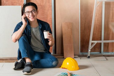 akıllı çekici gözlüklü Asyalı erkek zanaatkar ya da iç tasarımcı rahatlayın akıllı telefon konuşmaları site yorumlama ev iç tasarım yenileme ve geliştirme konsepti çalışıyor