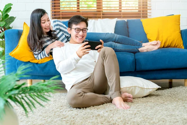 幸福的亚洲人甜蜜的夫妻在客厅的室内环境里一起玩智能手机的游戏 — 图库照片