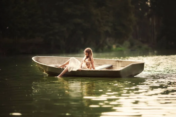 小女孩带着一只小狗在湖面上的一条小舟上沐浴着光芒 — 图库照片