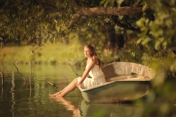 夏のドレスを着た若い女の子が日光の下で湖の上のボートに座っている — ストック写真
