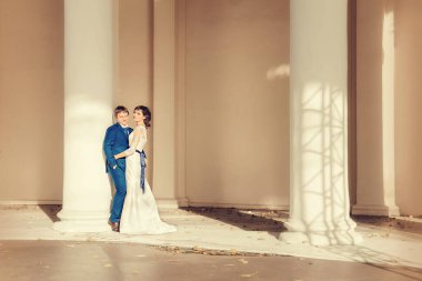 Düğün, yeni evliler güneş ışınlarında sütunları olan beyaz bir odada duruyorlar.