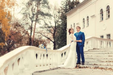 Düğün, yeni evliler sonbahar parkında beyaz sütunlarla merdivenlerde duruyorlar.