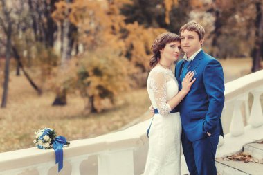 Düğün, yeni evliler sonbahar parkında beyaz sütunlarla merdivenlerde duruyorlar.