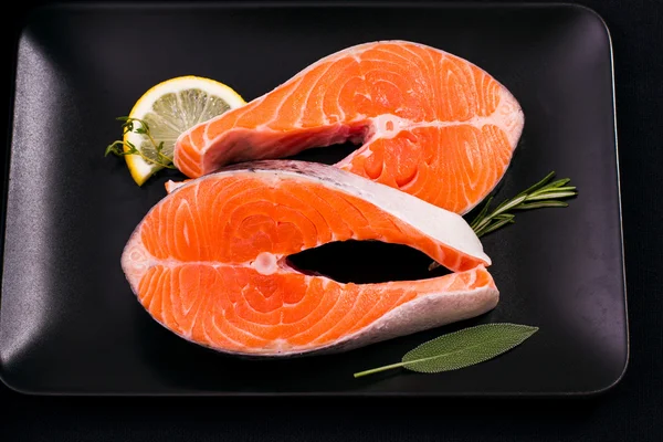 Due deliziose fette di salmone crudo su piatto nero — Foto Stock