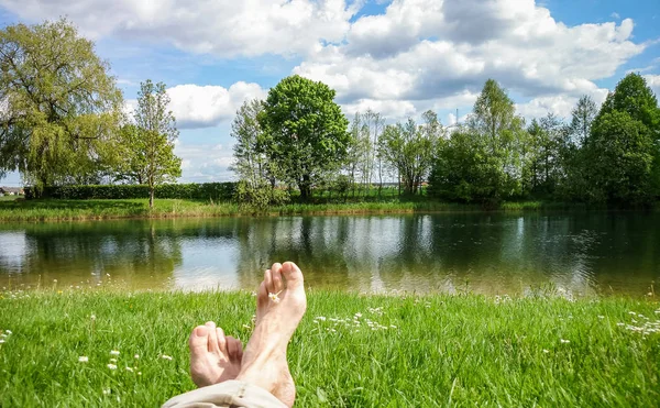 Pernas e pés relaxantes na frente da lagoa de água doce serena — Fotografia de Stock