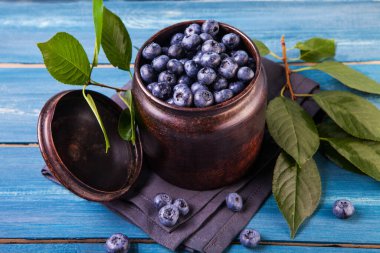 Metal kasede taze toplanmış yabanmersini. Mavi ahşap masada yeşil yapraklı sulu ve taze yabanmersini. Ahşap arka planda yabanmersini. Yabanmersinli antioksidan. Sağlıklı yeme ve beslenme kavramı.