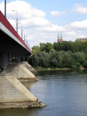 Varşova, Polonya - 09.11.2019: Vistula Nehri üzerinde bir köprü, ufukta ağaçların üzerinde iki keskin piramit kulesi var.