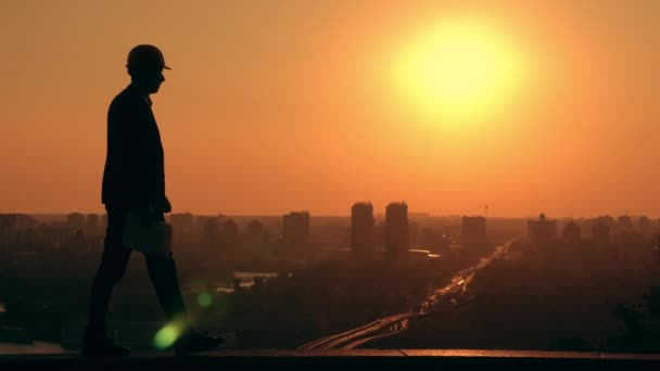 Zakenman in een harde hoed holding plan stadsgezicht bij zonsopgang — Stockvideo