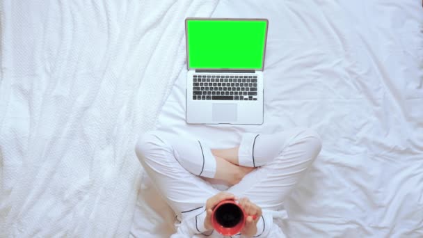 Vista sopra femmina tenendo tazza rossa guardando sul computer display si siede in camera da letto — Video Stock