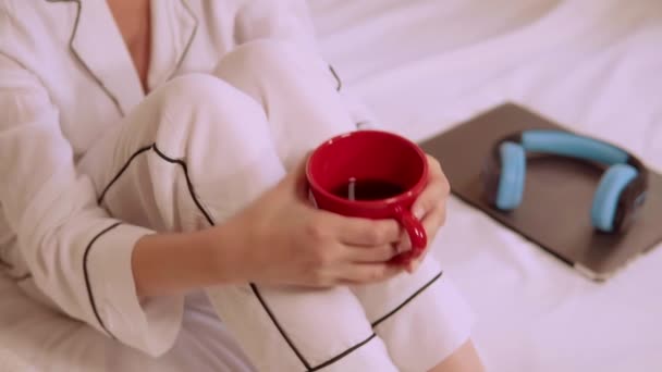 Zbliżyć się kobieta w białej piżamie delektować kawy w sypialni — Wideo stockowe