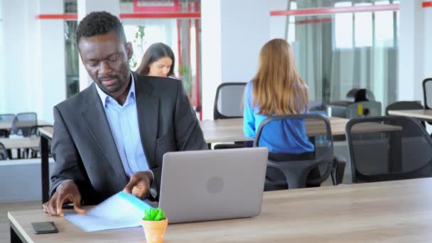 Афроамериканський менеджер, що тримає теку з документами, працює у відкритому офісі працівника стартап-компанії — стокове відео