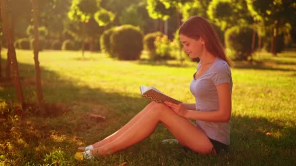 Fröhliche Frau liest Roman sitzt im grünen Gras — Stockvideo