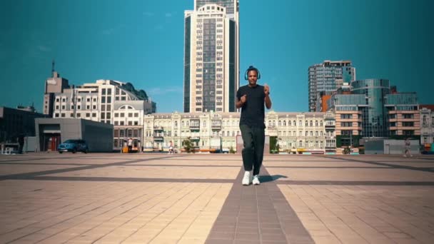 Chico en ropa de moda escuchando música caminando en la ciudad — Vídeos de Stock